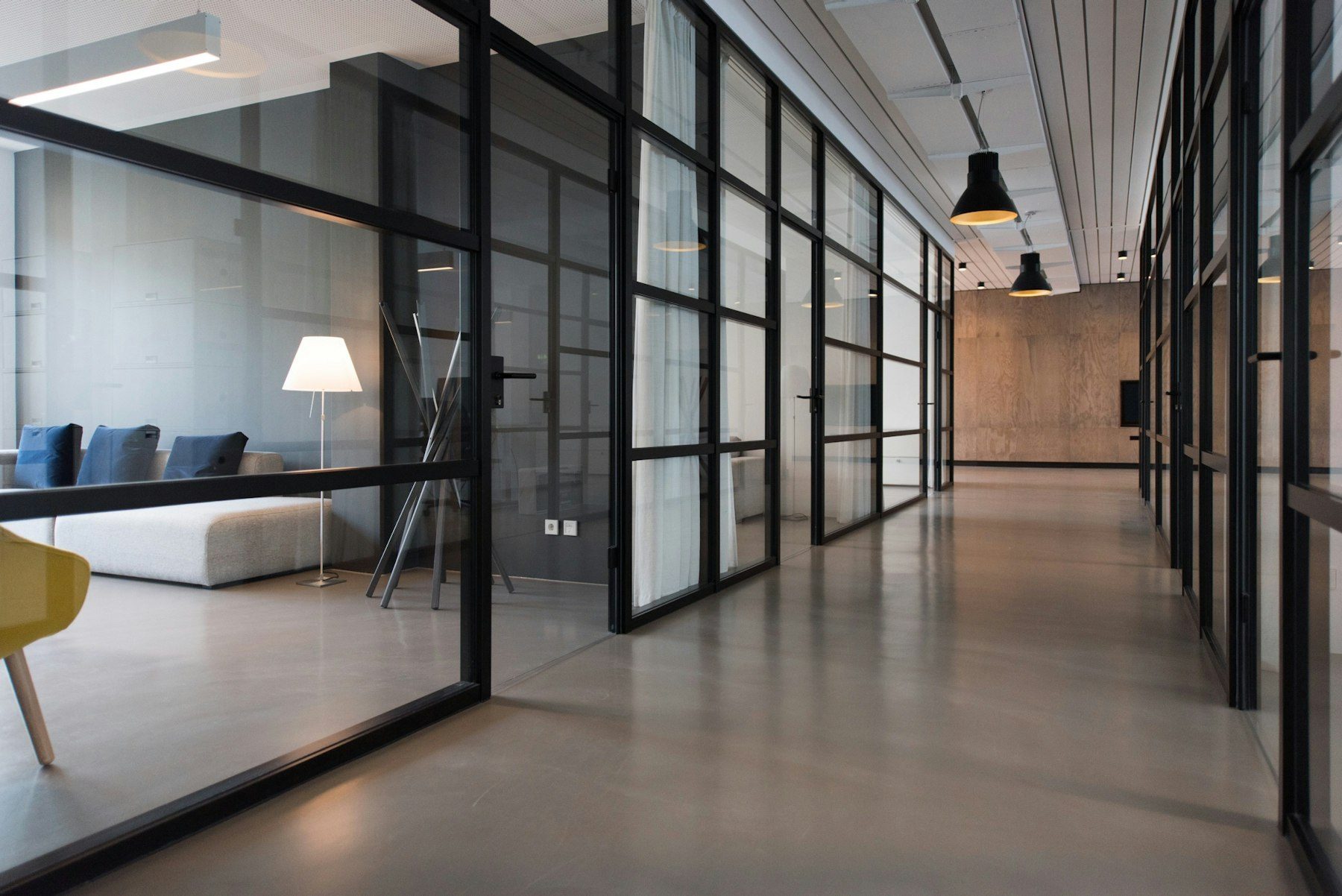 Interior corridor of a modern commercial office building with glass-partitioned offices and meeting rooms